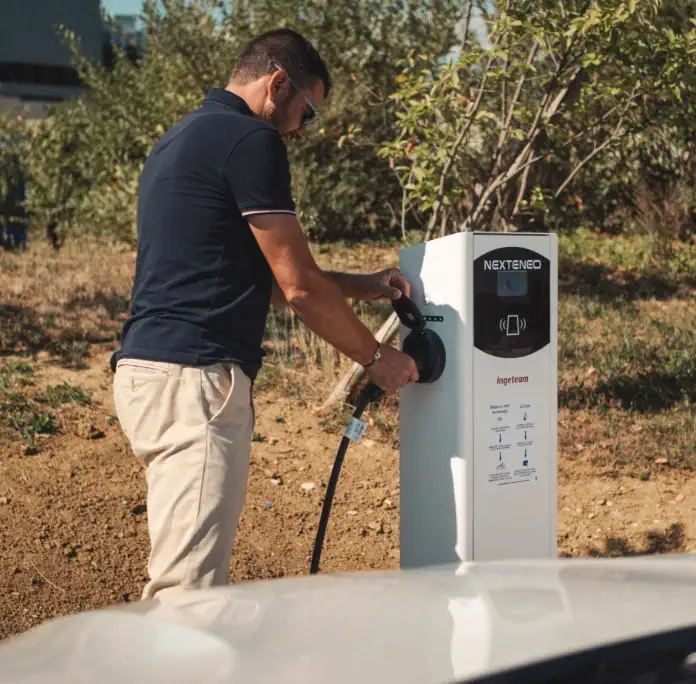 Un homme branche son véhicule électrique ou hybride à une borne de recharge Nexteneo située dans un parc de bornes