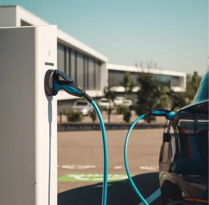 Vue rapprochée d'une borne de recharge Nexteneo avec un câble bleu connecté à une voiture électrique. En arrière-plan, un parking équipé d'un parc de bornes