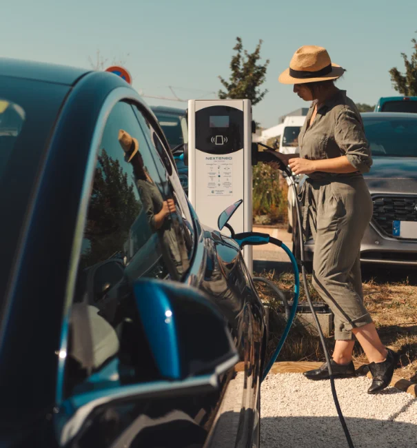 Femme branchant sa voiture électrique ou hybride à une station de recharge innovante Nexteneo