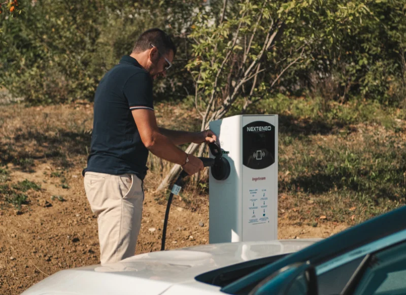 Un homme branche sa voiture électrique à une borne intelligente de recharge Nexteneo située en Savoie