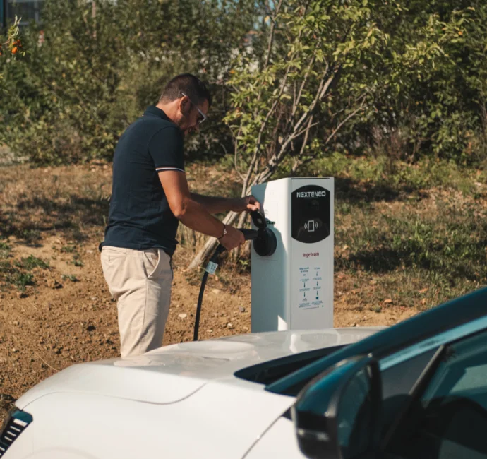 Un homme branche sa voiture électrique ou hybride à une station électrique de recharge Nexteneo située dans un parc de bornes
