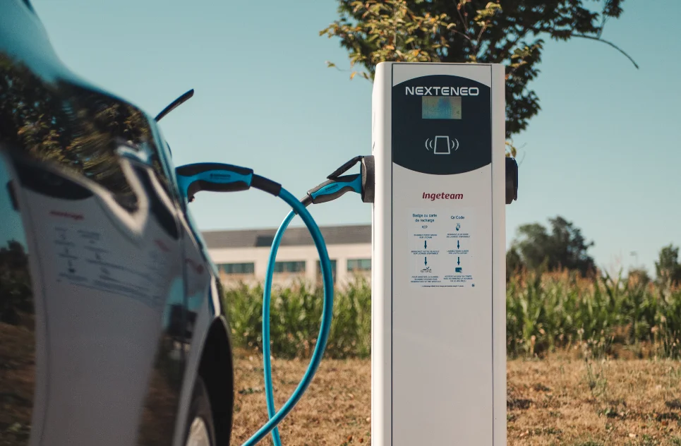 Véhicule hybride en train de se recharger à l'aide d'une borne Nexteneo sur un parc de bornes de recharge. La technologie Ingeteam est mise en évidence sur la borne ainsi que des conseils d'utilisation.