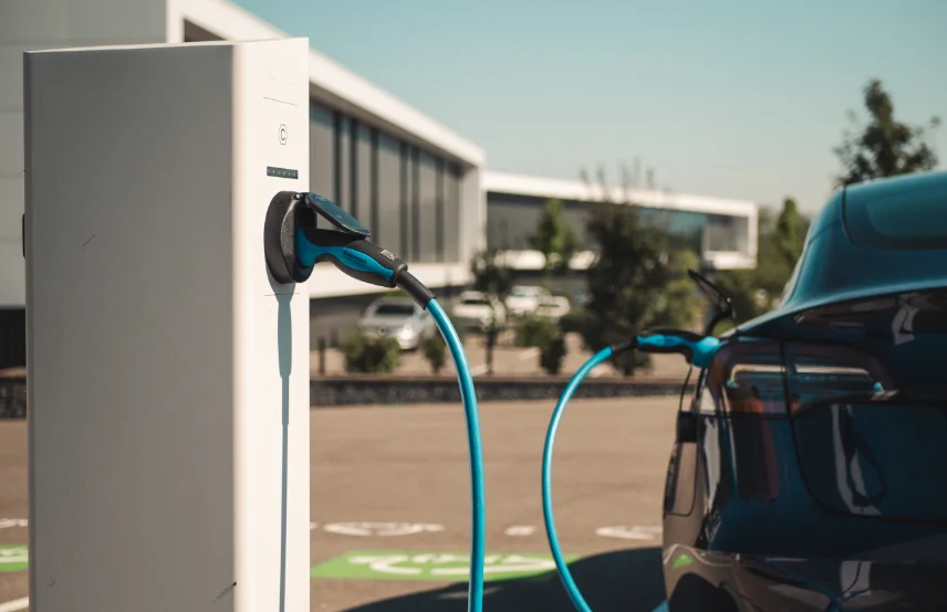 Vue rapprochée d'une station de recharge intelligente Nexteneo avec un câble connecté à une voiture électrique ou hybride. En arrière-plan, un parking équipé d'un parc de bornes connectées