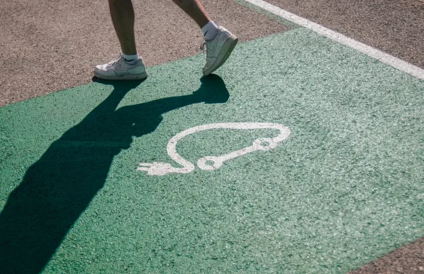 Personne marchant sur un emplacement de stationnement dédié aux véhicules électriques et hybrides pour l'alimentation via une station de recharge.