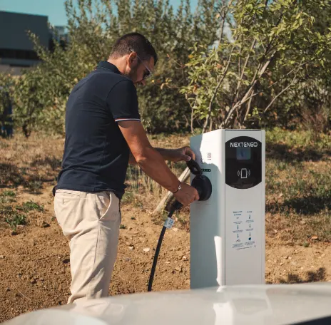 Un homme branche sa voiture électrique ou hybride à une station électrique de recharge Nexteneo située dans un parc de bornes