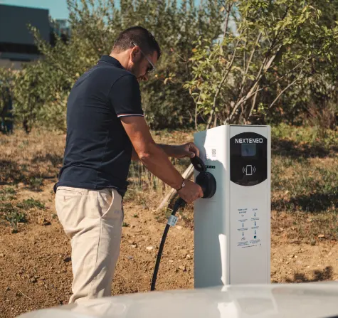 Un homme branche sa voiture électrique ou hybride à une station électrique de recharge Nexteneo située dans un parc de bornes