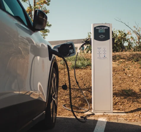 Véhicule hybride en train de se recharger à l'aide d'une borne Nexteneo sur un parc de bornes de recharge. Les conseils d’utilisation sont mise en évidence sur la borne.