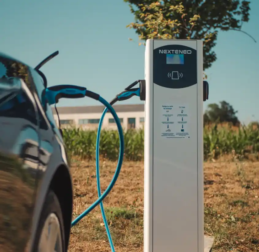 Véhicule électrique en train de se charger à l'aide d'une station Nexteneo sur un parc de bornes de recharge. La technologie Ingeteam est mise en évidence sur la borne connectée.